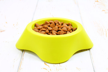 Yellow-green bowl with dry cat food on a white wooden floor