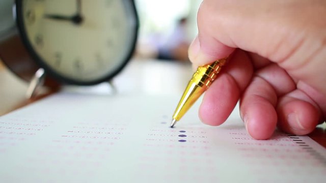 Asian Students taking optical form of standardized exams near Alarm clock with hand holding yellow pen for final examination in secondary school, college university classroom, Education concept