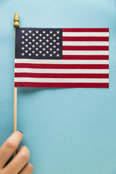 Close-up of woman's hand holding American flag against blue background