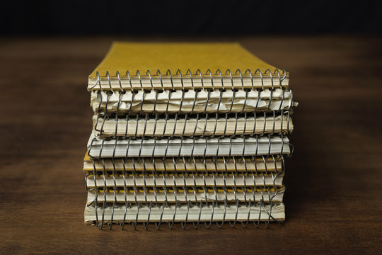Old used reporter's notebooks stacked on a wooden table.