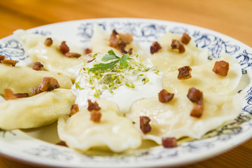 Cooked dumplings with cheese pork scratching and creme fraiche on wooden table.
