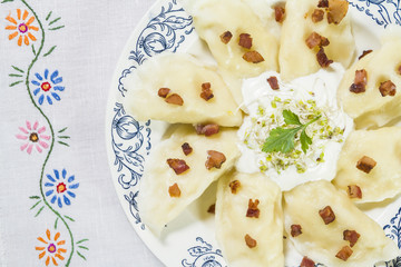 Cooked dumplings with cheese pork scratching and creme fraiche on wooden table.
