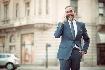Smart senior business man, an elderly entrepreneur and business owner, talking over his cell phone in an outdoors urban area