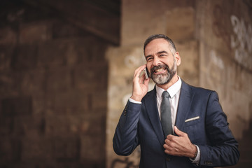 Smart senior business man, an elderly entrepreneur and business owner, talking over his cell phone in an outdoors urban area