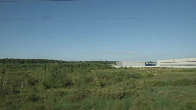 POV: High-speed Train moves near a forest, field and warehouse