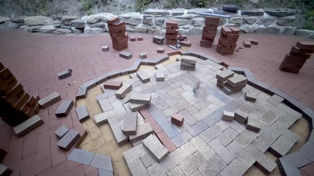 Steadicam shot rotating around a custom designed hardscaping brick paving emblem under construction as the paving expert comes over to fit a brick into place.