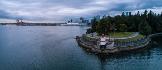 Fototapeta premium Brockton Point Lighthouse in Stanley Park, with Vancouver Downtown, BC, Canada, in the background. Taken during a cloudy morning sunrise. Aerial Panorama