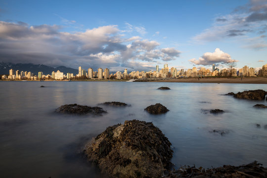 Long exposure view from the rocky beach of Downtown Vancouver, BC, Canada, during sunset.