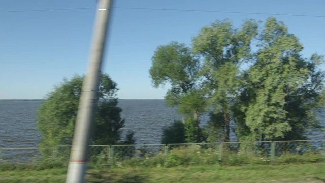 POV: High-speed Train moves past a lake and trees on a coast in a sunny day