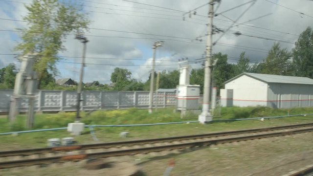 POV: High-speed Train fast moves past a railway station in a town - clouds in a sky