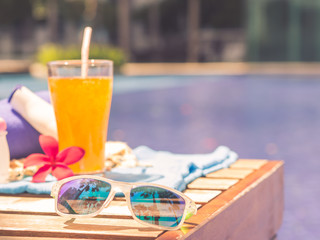 Retro style sungrasses, shampoo, lotion, hat, rolled up towels and Orange juice at the side of swimming pool. Vacation, beach, summer travel concept