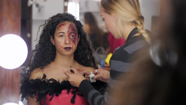 Make-up artist make the girl halloween make upin studio.Halloween face art.Woman applies on professional greasepaint on the face of spanish girl.War-paint with blood, scars and wounds.Slow motion.