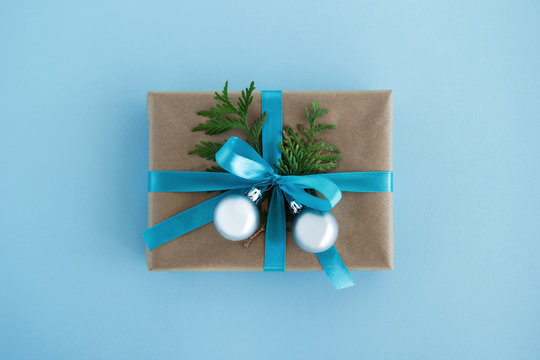 Gift box wrapped of craft paper, blue ribbon and decorated fir branches and silver Christmas balls on the blue background, top view. Christmas present.
