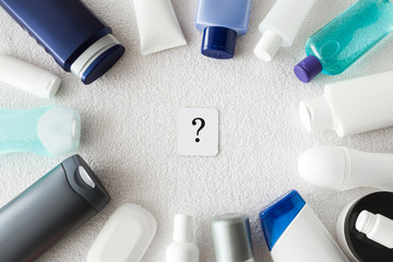 Different, colorful beauty toiletries with sign of question on the white towel. Cares about a men's and women's hair and body skin. The concept of choice and indecisiveness. Top view. - obrazy, fototapety, plakaty