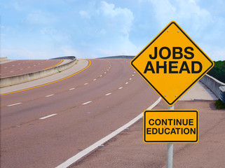Road sign with a wonderful and powerful message of success that says JOBS AHEAD CONTINUE EDUCATION with a winding road leading up to a beautiful blue sky in the background with ample copy space.