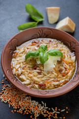 Closeup of italian soup with lentil, pasta and addition of parmesan served in a clay plate