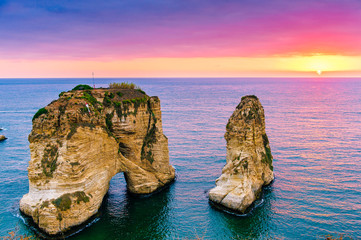 Naklejka premium Piękny zachód słońca na Raouche, Pigeons 'Rock. W Bejrucie w Libanie Słońce i kamienie odbijają się w wodzie, gęste chmury na niebie.