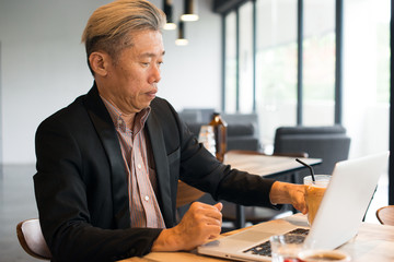 asian senior male using laptop on cafe