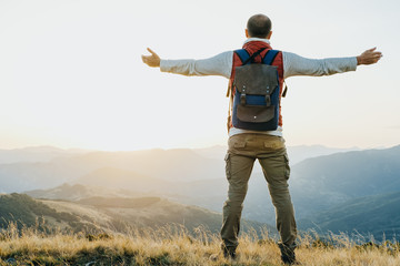 Hiker with backpack standing and rasing his hands at mountain background
