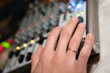 DJ working on a audiomixer at a nightclub. Close-up of hands adjusting quality of music using a...