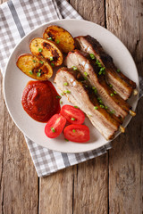 Delicious roast pork brisket with potato skins, tomatoes and sauce close up. vertical top view