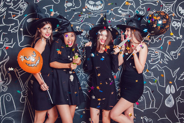 Beautiful girls in witches costumes blow up confetti on a dark background with a picture. Halloween.