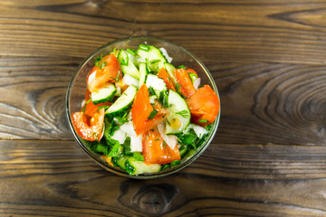 Fresh salad with tomato, cucumber, onion, parsley and dill in glass bowl on wooden table