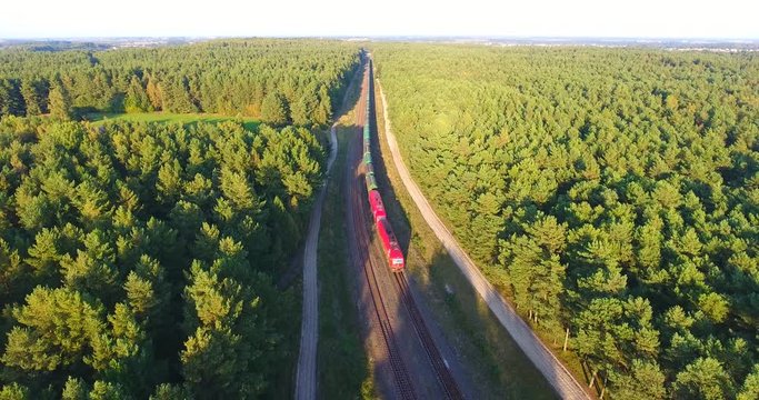 - AERIAL railway: Long cargo train transporting wagons across the autumn forest at sunset