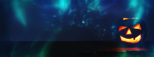 Halloween Pumpkin on wooden table in front of spooky dark background. Jack o lantern