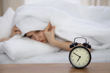 Beautiful sleeping woman lying in bed and trying to wake up with alarm clock. Girl having trouble...
