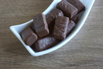 Chocolate candies in plate. Sweet black chocolate pieces.
