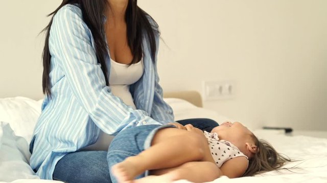 Happy asian mother tickles her daughter on bed at home