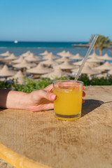 A woman's hand holds a straw. Glass of fresh orange juice against the sea