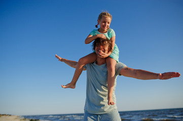 Young man gaily spends time with the little daughter by the sea.