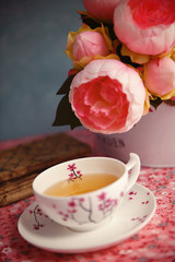 A cup of tea, old books and peonies on a table