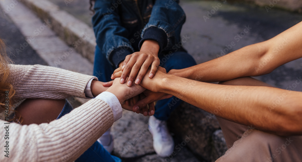 Wall mural group of friends sitting together stacking their hands on one an