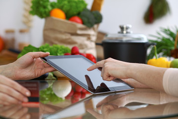Close-up of human hands pointing into tablet  in the kitchen. Friends having fun while choosing...