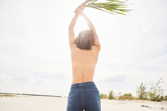 An asian girl topless walking around a beach on sand in backlight with a bunch of grass