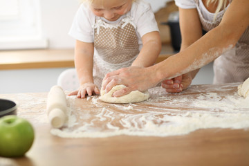 Mother and her cute daughter hands prepares the dough on wooden table. Homemade pastry for bread or pizza. Bakery background