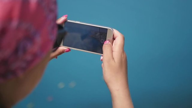 A girl in a pink bandana takes pictures of a deep blue sea on her phone. Slow Motion. HD, 1920x1080..