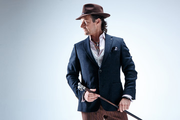 The mature man in a suit and hat holding cane.