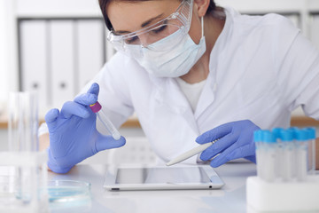 Close-up of professional female scientist in protective eyeglasses making experiment with reagents in laboratory. Medicine and research concept