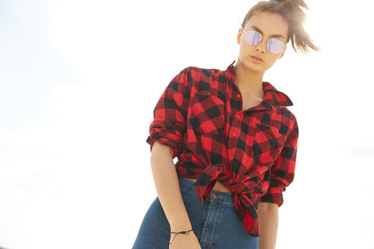 Asian girl in sunglasses and red squared shirt and blue jeans in the sun