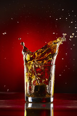 Close-up of glass with whiskey splash.On red background.Concept alcohol splash