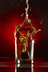 Close-up of glass with whiskey splash.On red background.Concept alcohol splash