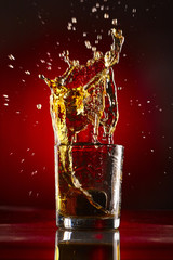 Close-up of glass with whiskey splash.On red background.Concept alcohol splash