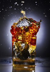 splash of whiskey with ice.Grey background.Concept alcohol splash