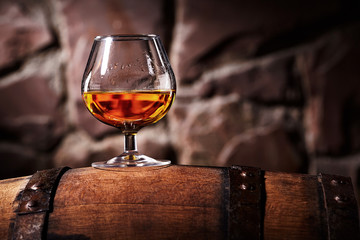 Glass of cognac on the old wooden barrel - obrazy, fototapety, plakaty