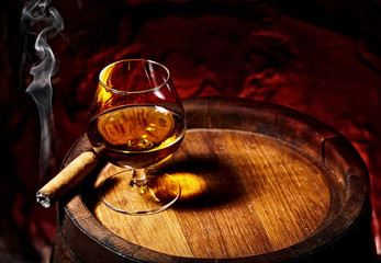 Cognac and Cigar on old oak barrel.Red stone background