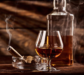 Glass of cognac or brandy with smoking cigar on wooden table